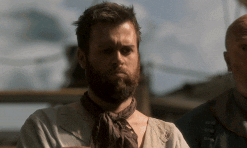 a man with a beard and a scarf around his neck stands next to another man