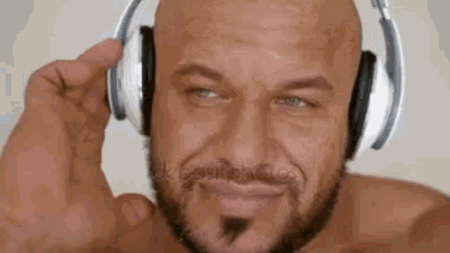 a bald man with a beard is listening to music with headphones .