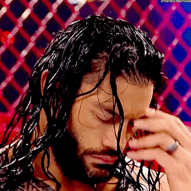 a man with long black hair and a beard is covering his face with his hands .
