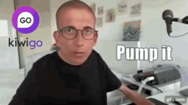 a man wearing glasses and a black shirt is standing in front of a microphone and a sign that says kiwigo pump it