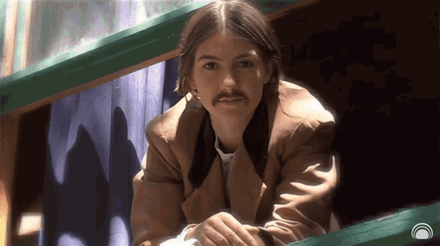 a man with long hair and a mustache looks out of a window