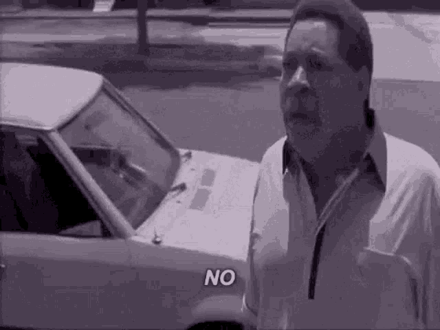 a man is standing in front of a white car and saying `` no '' .