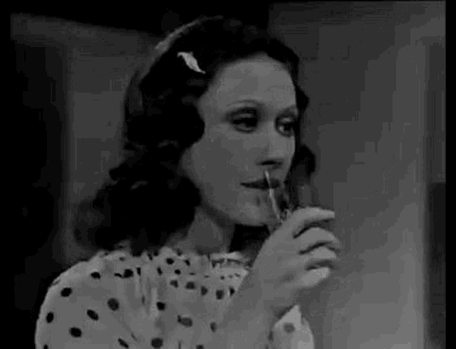 a woman in a polka dot shirt is drinking a glass of water .