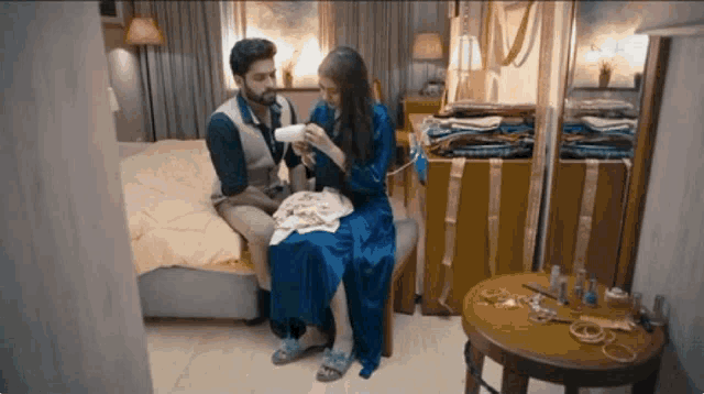 a man and a woman are sitting on a bed in a bedroom . the woman is wearing a blue robe .