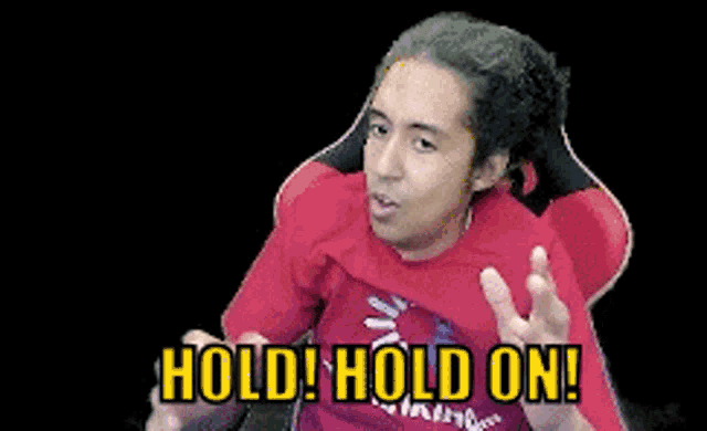 a man in a red shirt is sitting in a chair and says hold hold on .