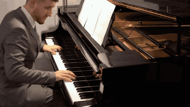 a man in a suit is playing a piano with sheet music on it