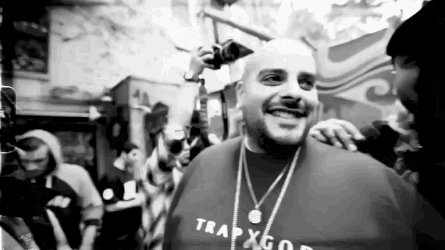 a man wearing a trap god shirt is smiling in a black and white photo