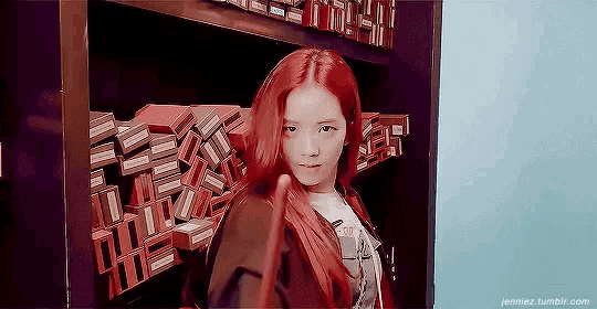 a girl with red hair is standing in front of a bookshelf .