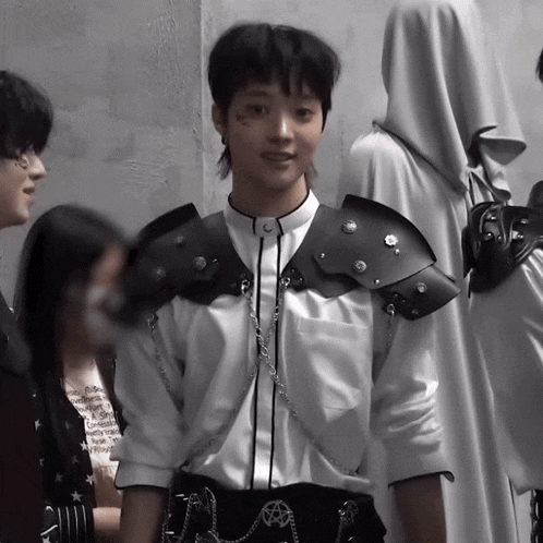 a man wearing a white shirt and black armor stands in front of a wall