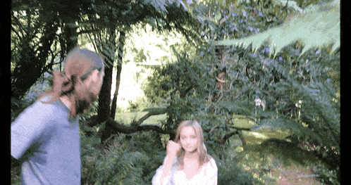 a man and a woman are standing in a forest with trees in the background