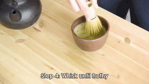 a person is whisking a bowl of green tea on a table .