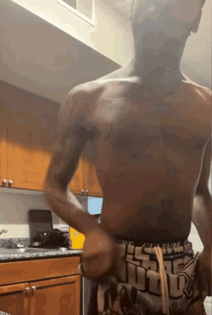 a shirtless man is standing in a kitchen wearing a pair of underwear with the word culture on them