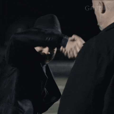 a man in a suit and hat shakes hands with another man in a black jacket