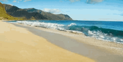 a sandy beach with mountains in the background and waves crashing on the shore