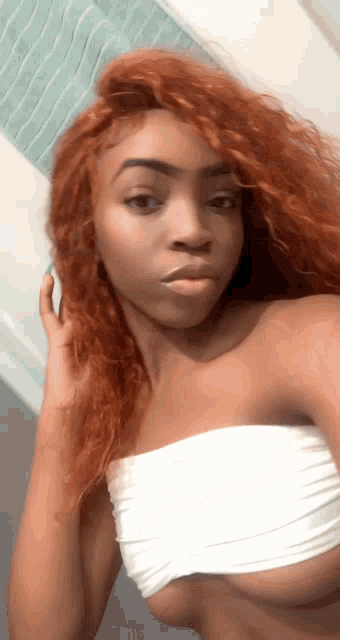 a woman with red hair is taking a selfie in a white tube top