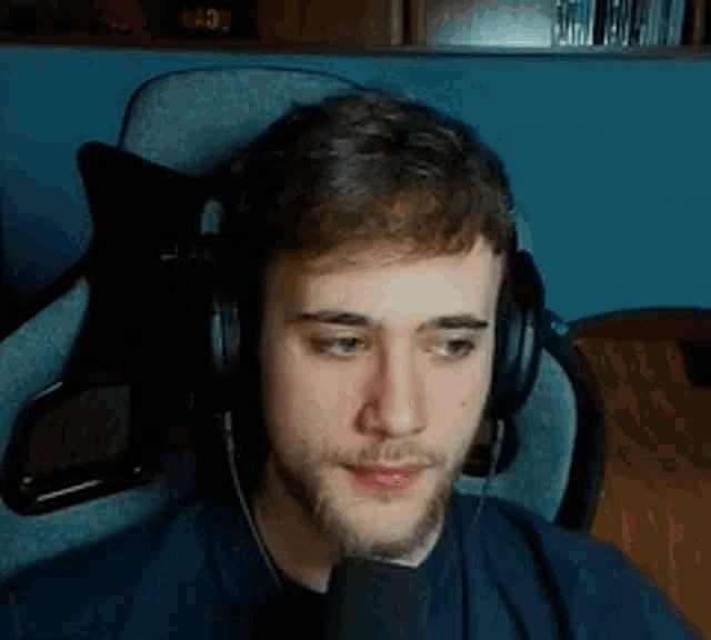 a young man with a beard is wearing headphones and a microphone while sitting in a chair .