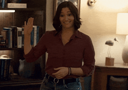 a woman in a maroon shirt and jeans is waving her hand