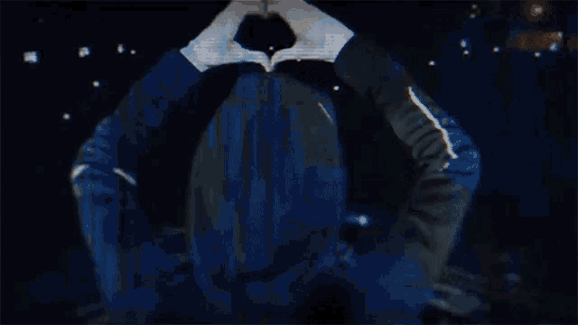 a person is making a heart shape with their hands in the dark .