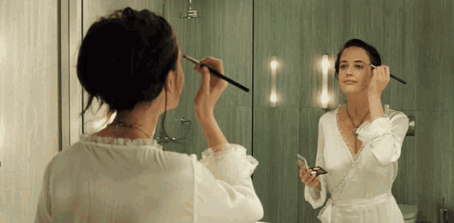 a woman applying makeup in front of a bathroom mirror