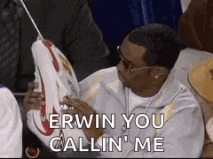 a man is sitting in a stadium holding a pair of shoes and says `` erwin you callin ' me '' .