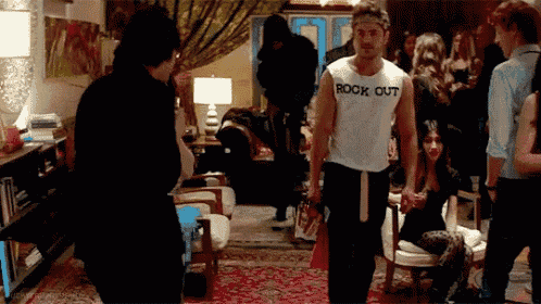 a man wearing a white tank top that says rock out is standing in a crowded room .