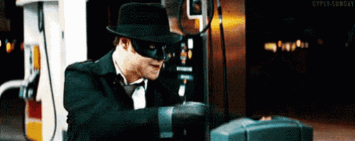 a man wearing a mask and hat is standing in front of a gas pump .
