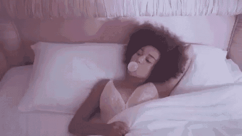 a woman is blowing a bubble of gum while laying in bed .