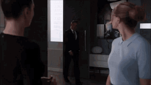 a man in a suit and tie is standing in a doorway talking to two women .