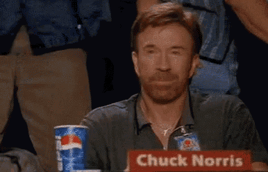 chuck norris is sitting at a table with his fist in the air .