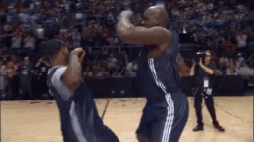 two basketball players are dancing on the court while a cameraman takes a picture of them .