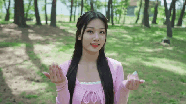 a girl in a pink sweater is standing in a park with her hands in the air .