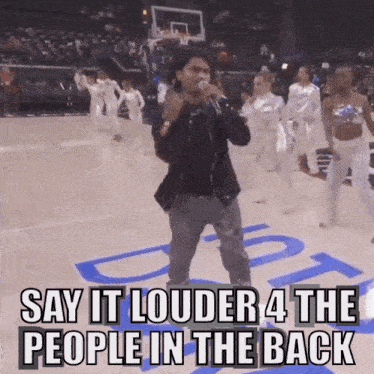 a man singing into a microphone with the words say it louder 4 the people in the back behind him