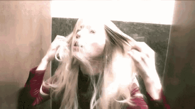 a woman with blonde hair is looking at herself in a mirror .