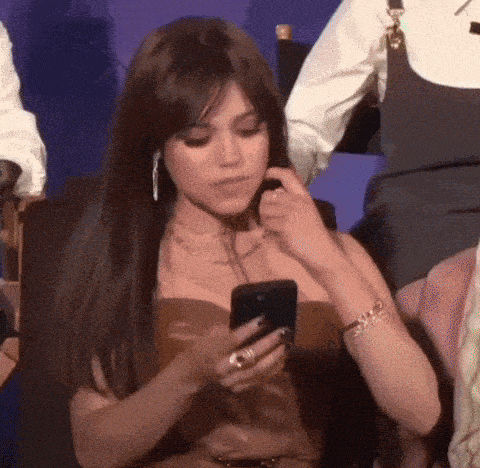 a woman in a brown dress is sitting in a chair looking at her cell phone .