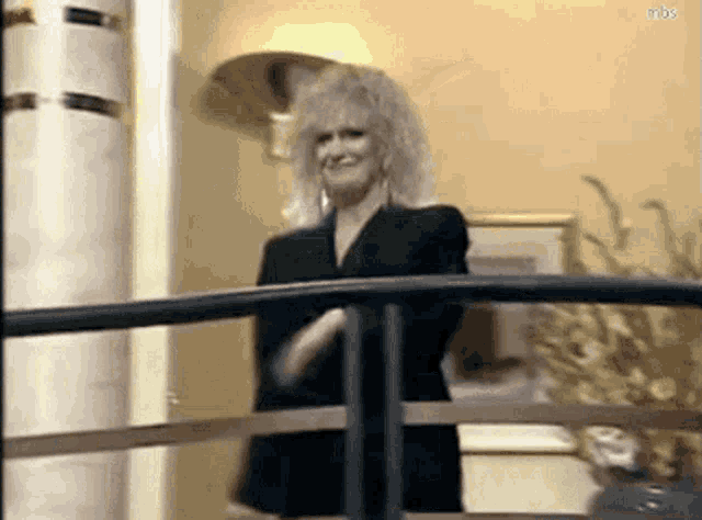 a woman in a black suit is standing on a balcony with her arms crossed .