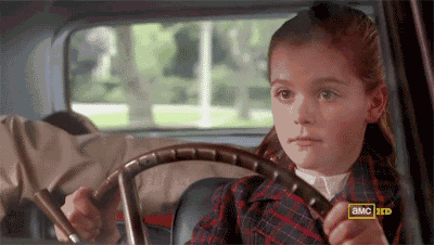 a little girl is sitting in the driver 's seat of a car holding a steering wheel .