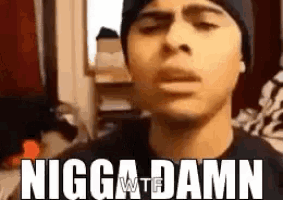 a man wearing a beanie is making a funny face with the words nigga damn written on his face .