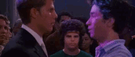two men are standing next to each other in a crowded room and talking to each other .