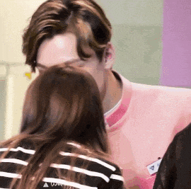 a man in a pink jacket is kissing a woman on the back of her head .