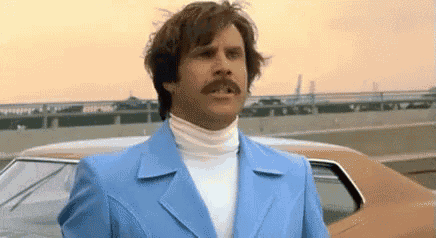 a man in a blue suit and white turtleneck is standing next to a car .