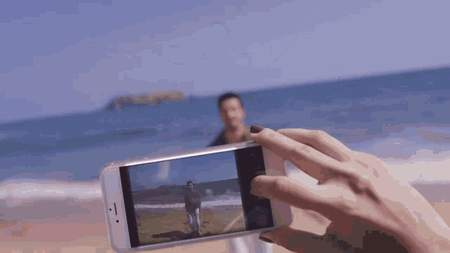 a person taking a picture of a man on the beach with their phone