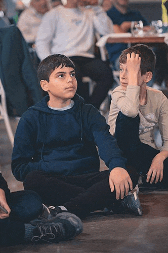 two young boys are sitting on the floor with their hands on their head