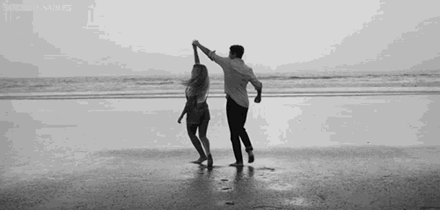 a man and a woman are dancing on the beach in a black and white photo .