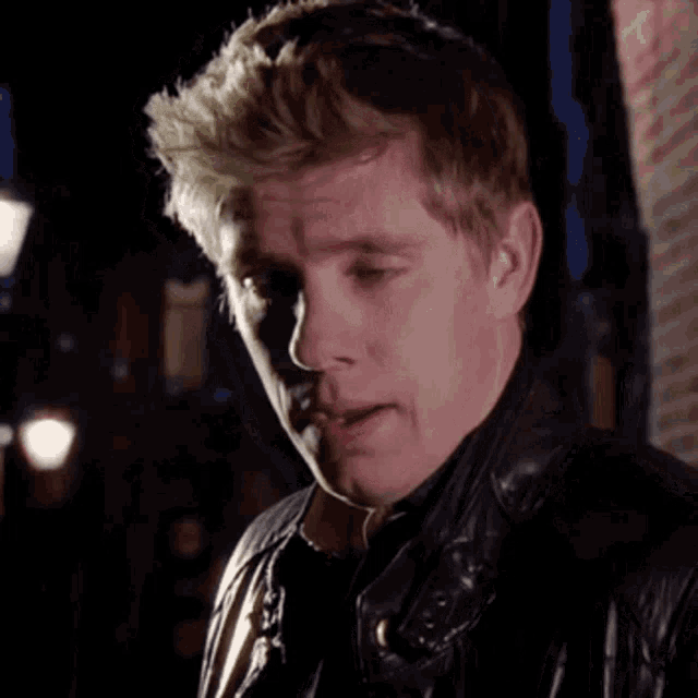 a man wearing a leather jacket looks down with his eyes closed