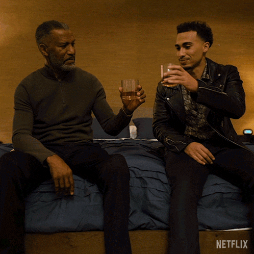 two men are sitting on a bed toasting with netflix written on the bottom
