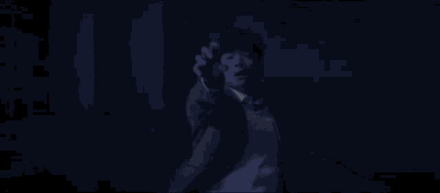 a man in a suit and tie is standing in the dark holding a gun .