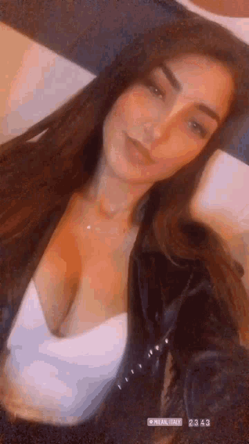 a woman in a white top and a black jacket is taking a selfie with her phone .