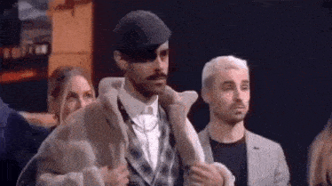 a man with a mustache and a hat is standing next to a woman in a crowd of people .