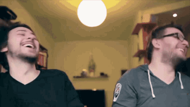 two men are laughing in a room and one has a patch on his sleeve that says ' a ' on it