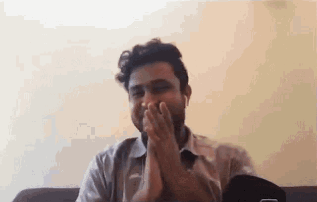 a man is sitting on a couch with his hands folded and covering his mouth .